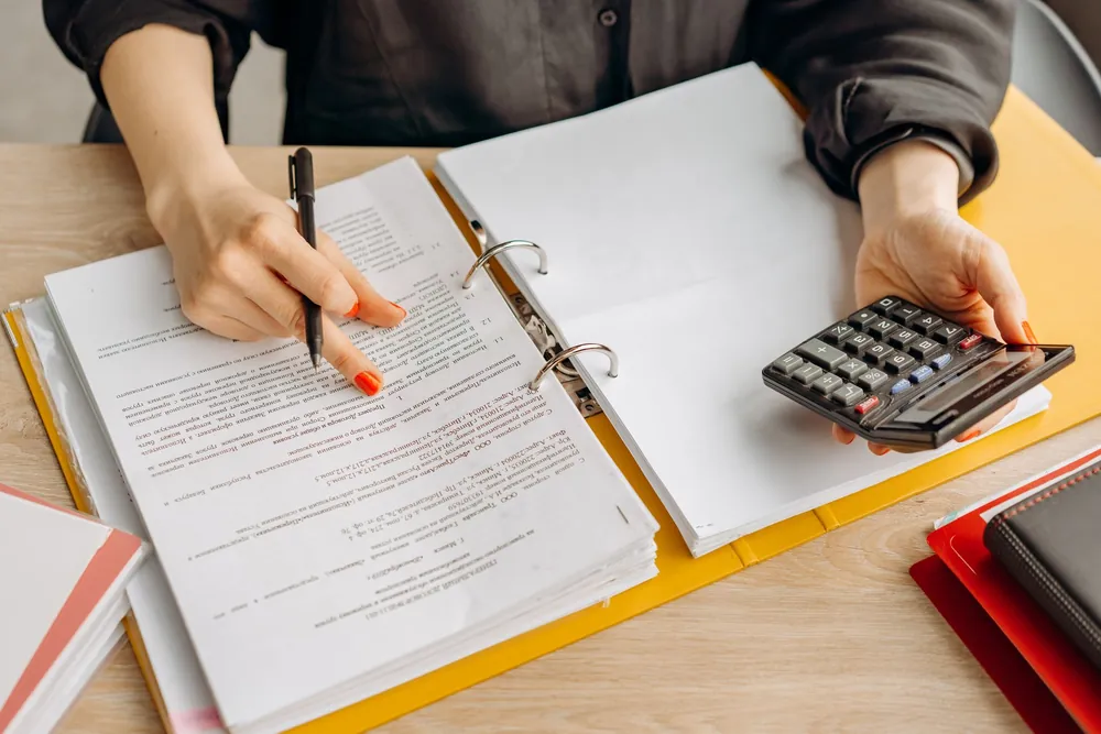 Une femme consulte des documents en utilisant une calculatrice sur son bureau
