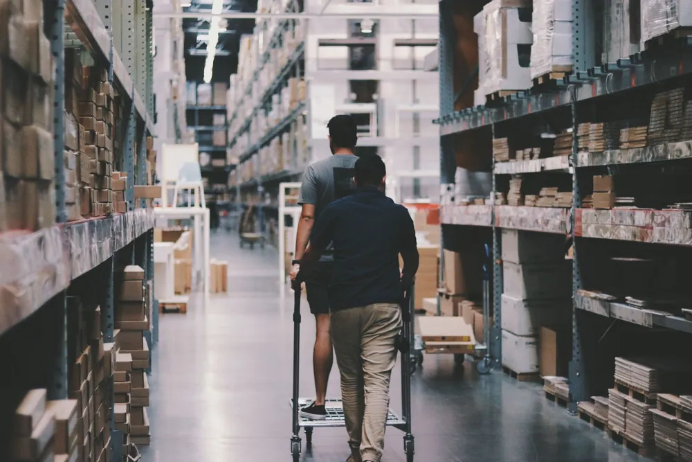 Deux employés manient un chariot dans un entrepôt logistique rempli de cartons
